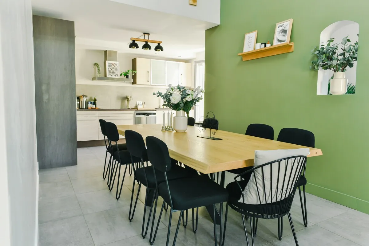Salle à manger avec grande table conviviale et mur vert